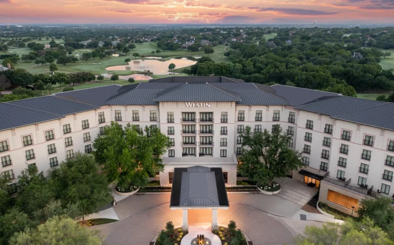 Aerial view of the Westin hotel surrounded by trees and a golf course at sunset, with a vibrant sky in the background.