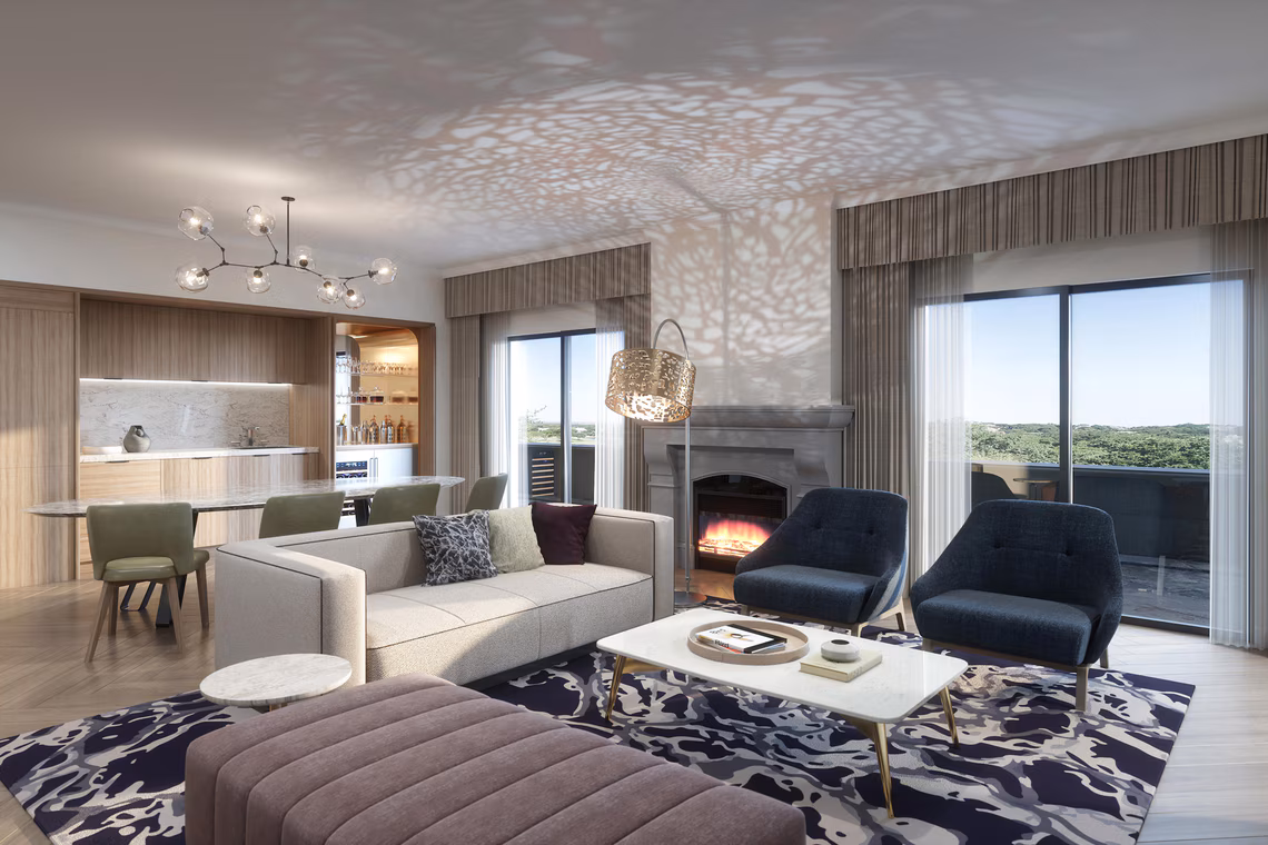 Modern living room with a sofa, two chairs, fireplace, coffee tables, and a dining area, with large windows showing a scenic outdoor view.