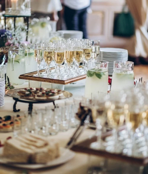 A table set with champagne glasses, pitchers of lemonade, plates of appetizers, and a cake, ready for a celebration or reception.