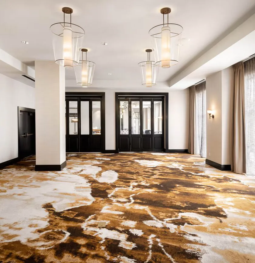 Modern empty room with abstract brown and white carpet, large windows with sheer curtains, pendant lights, and double black doors.